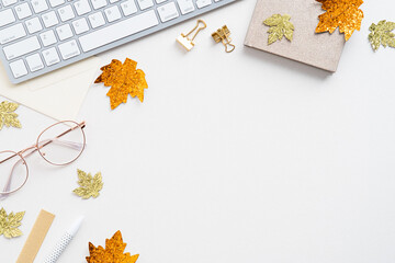 Autumn desk table with golden maple leaves, keyboard, female glasses on white background. Flat lay, top view, overhead.
