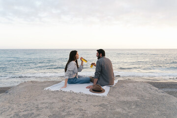 Fototapeta na wymiar Couple enjoying seaside view, drinking beer alone. Portrait of happy people spending time picnic leisure together on the sunset.
