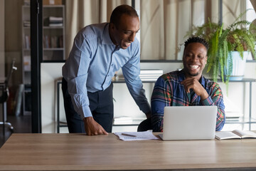 Happy Black office employees of different ages looking at laptop screen at workplace, laughing, having fun. African American coworkers reading email, making video call, watching presentation - Powered by Adobe