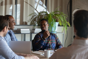 Happy African American hipster worker speaking on meeting, discussing project with coworkers,...