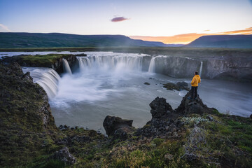 The aerial view of a man hiker enjoying beautiful waterfall of Godafoss at sunset light. Iceland in the summer season