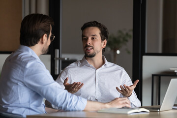 Two office employees meeting and working at workplace laptop, talking, discussing project. Mentor...