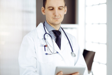 Friendly male doctor using tablet computer in sunny clinic. Medicine and healthcare concept - 459277930