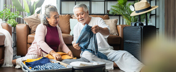 old asian senior couple packing cloth and stuff for a trip together,happiness asian old age retired mature adult enjoy arrange cloth together on floor at living room at home interior background