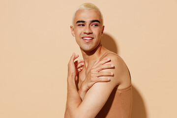 Side view young smiling fun blond latin hispanic gay man with make up in beige tank shirt hug...