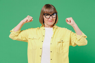 Elderly strong sporty fitness happy woman 50s in glasses yellow shirt show hand biceps muscles...