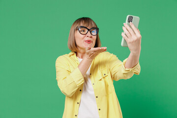 Elderly smiling happy woman 50s in glasses yellow shirt doing selfie shot on mobile cell phone post...