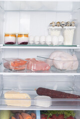 Fototapeta na wymiar in the open refrigerator, on glass shelves, there are products, whole chicken, meat, eggs, cheese, sausage, cottage cheese ,yogurt and vegetables