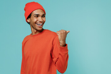 Young smiling happy fun african american man 20s in orange shirt hat point thumb finger back aside...