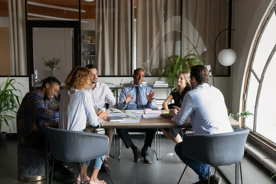 African American business leader talking to team of employees at office meeting, discussing work project at table. Mentor training diverse group of interns, explaining tasks, giving instructions