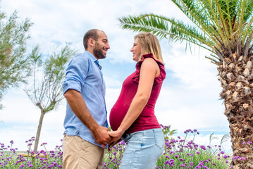 happy couple in love of a pregnant woman and her boyfriend holding hands looking into each other eyes outdoors. quality family time holding hands on vacation days. joy, big belly and lifestyle concept