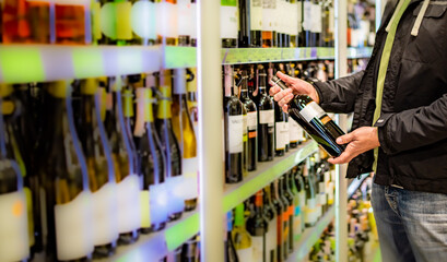 man hand holding bottle wine in grocery store in supermarket