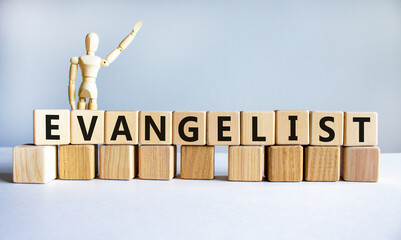 Evangelist symbol. The word Evangelist on wooden cubes. Wooden model of human. Businessman icon. Beautiful white background. Business and evangelist concept. Copy space. - obrazy, fototapety, plakaty