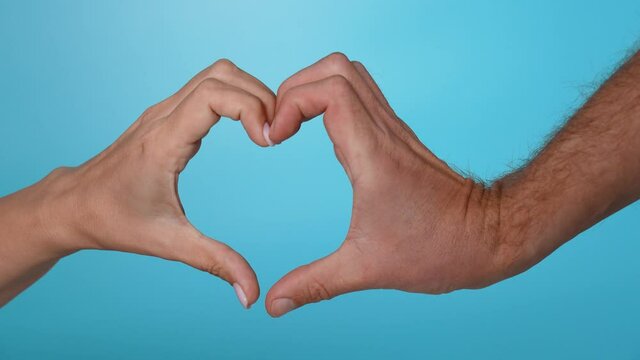 Closeup view 4k slow motion video footage of two human hands making love symbol gesture forming heart shape with their fingers. Man and woman touching each other with tenderness and love
