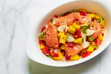Spicy salmon mango salad in white oval bowl. Top view on white table with copy space.