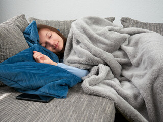Beautiful young woman wrapped in a soft blanket sleeping on the couch at home. The girl is taking an afternoon nap.