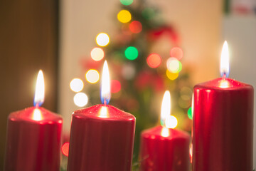 Four red candles burning on advent wreath with blurred colorful christmas tree with glowing lights in the background on evening. Merry Christmas, Advent crown decoration, 4th sunday, Xmas backdrop