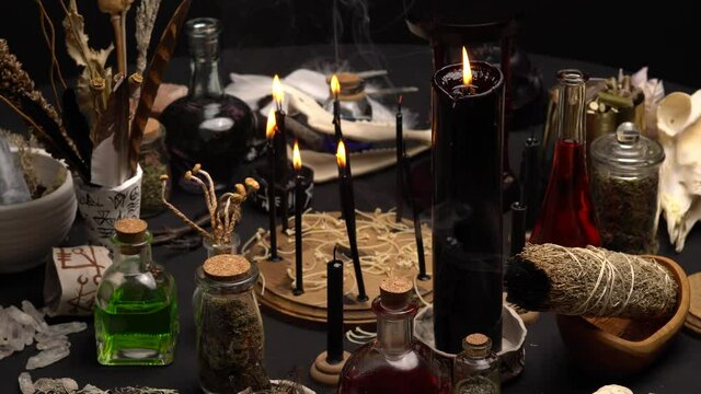 Occult and esoteric witch doctor still life. Halloween background with magic objects. Black candles, skull, bones, and potions vials on witch table. Mystic witchery with weeds. Halloween concept.