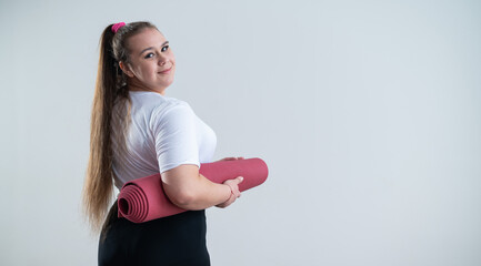 Young fat caucasian woman holding a sport mat. Charming plus size model in sportswear stands on a...