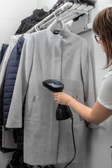 Wet heat treatment of clothes with steam. The woman is steaming a gray coat with a handheld...
