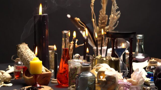 Occult and esoteric witch doctor still life. Halloween background with magic objects. Black candles, skull, bones, and potions vials on witch table. Mystic witchery with weeds. Halloween concept.