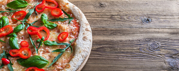 Margherita pizza with red pepper and fresh basil on a wooden table