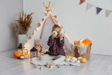 Little cute girl playing in a wigwam in her room with autumn decor and pumpkins. Happy childhood concept © Наталья Мокрецова