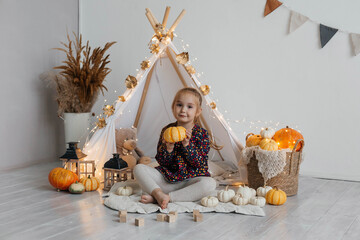 Little cute girl playing in a wigwam in her room with autumn decor and pumpkins. Happy childhood concept © Наталья Мокрецова