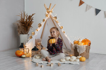 Little cute girl playing in a wigwam in her room with autumn decor and pumpkins. Happy childhood concept © Наталья Мокрецова