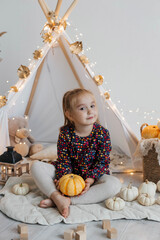 Little cute girl playing in a wigwam in her room with autumn decor and pumpkins. Happy childhood concept © Наталья Мокрецова