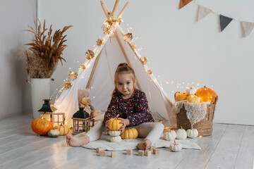 Little cute girl playing in a wigwam in her room with autumn decor and pumpkins. Happy childhood...