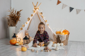 Little cute girl playing in a wigwam in her room with autumn decor and pumpkins. Happy childhood concept © Наталья Мокрецова