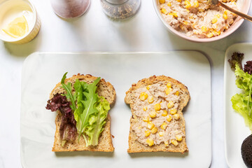 Preparing healthy sandwiches; super grains sliced bread, tuna, corn, avocado, lemon and vegetables on marble cutting board. Top view