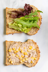 Preparing healthy sandwiches; super grains sliced bread, tuna, corn, avocado, lemon and vegetables on marble cutting board. Top view