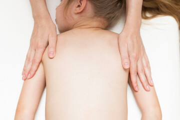 The hands of the masseur do a back massage for a girl of primary age. Spine. Back pain in school-age children.