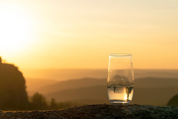 clean drinking water in a glass in the mountains, against the background of a beautiful evening sunset, copy space