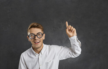 Portrait of smiling millennial Caucasian man in glasses on black studio background point at blank copy space above. Happy young male in spectacles recommend good sale deal or discount promotion.