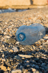 Plastic water bottle on a pebble beach. Plastic pollution. Wates on the beach.