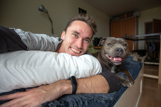 Pleased young man looking at camera and taking selfie with amstaff dog