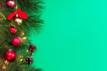 A branch of a Christmas tree with red and gold toy balls and cones isolated on a color green background with empty copy space for text or design. New Year's wallpaper. Fir tree frame
