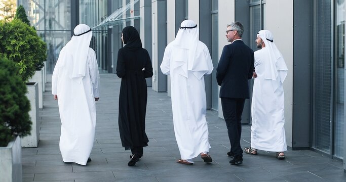 Full length view of the multi-ethnic group of business people are walking outdoors in city street talking with each other on sunny summer day. Cityscape and entrepreneurs concept
