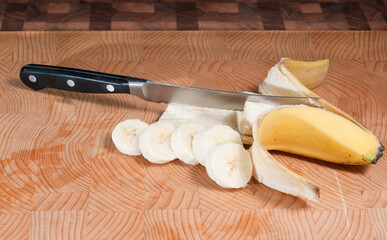 top, front view, medium distance of a pealed, ripe, banana sliced with a pairing knife on a wood cutting board