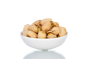 Several unpeeled pistachios in a white saucer, close-up, isolated on white.