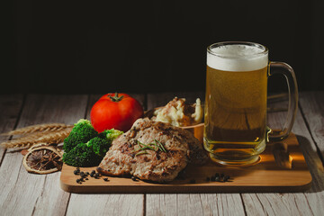 Barbecue dry aged rib of beef with rosemary, tomato, vegetables and a mug of cold light beer with foam for dinner. Vintage dark tone