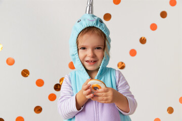 Cute little girl in narwhal costume holding cookie at home. Halloween party © Darya Lavinskaya