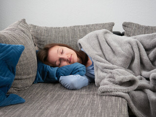 Beautiful young woman wrapped in a soft blanket sleeping on the couch at home. The girl is taking an afternoon nap.