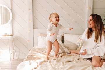 Smiling, having fun mom and daughter child spend time together playing on the bed by the Christmas tree on a holiday day in a cozy bedroom at home on the weekend. Selective focus