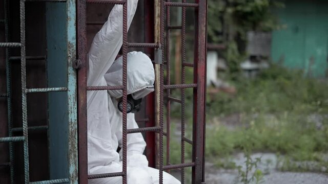 Man wearing protection suit, sitting in ruined constraction of building,exploring place and looking around
