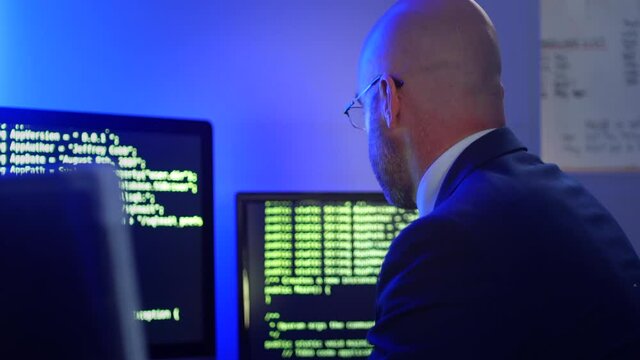 Software developer coding in an office on a computer with multiple screens showing code