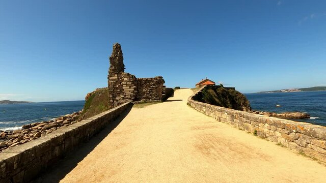 Traveling towards the peninsula where the La Lanzada beach chapel is located in Galicia, Spain, with ruins in the foreground. The sea is seen on both sides of the path way.